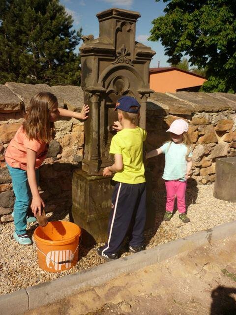 Děti čistí znovu postavený náhrobek v rámci revitalizace německého hřbitova při kostele sv. Jana Křitele. | Okrašlovací spolek Budíček | Všechna práva vyhrazena