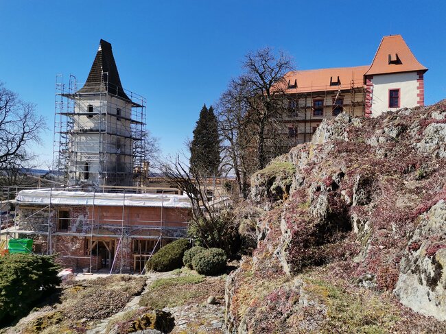 Hrad Kámen u Pacova – východní pohled přes skalní masiv na rekonstruovaný areál hradu s jižním předhradím tvořeným věží, přiléhající vstupní novogotickou branou a torzem bývalého pivovaru (stav z března 2025) | © Zlata Vobinušková