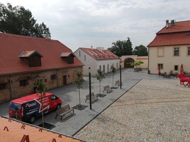 Pohled na dvůr Staré pošty, vlevo objekty s novými střechami a vpravo plastika koní připomínající historii místa