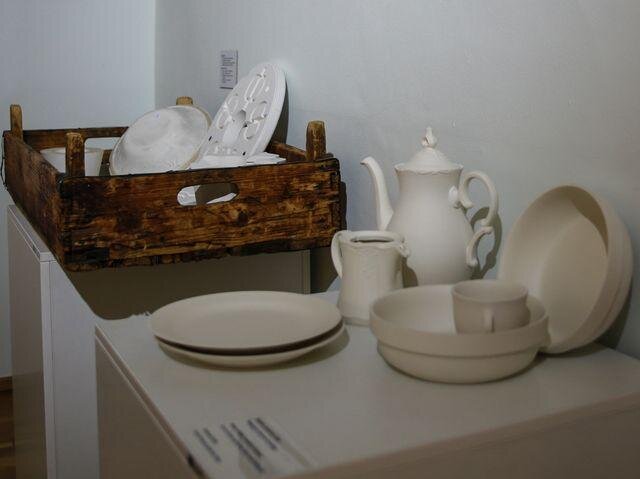 Na snímku vpředu vysušené polotovary z porcelánové výroby – vytvořené litím, točením a lisováním. V pozadí sádrové formy pro tvarování porcelánu