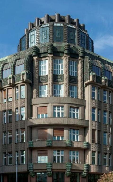 Nárožní pětipatrový palác se zaobleným nárožím a mansardovými podlažími je železobetonové konstrukce.